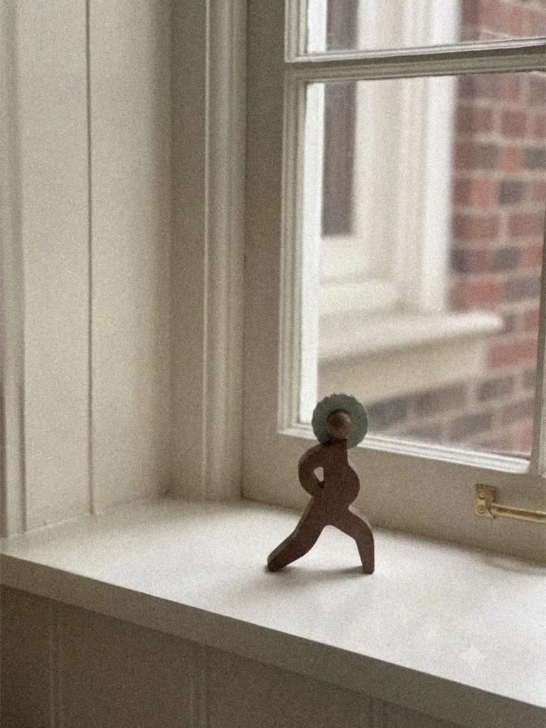 Kleine Holzfigur „Power" aus der Women & Moods Kollektion von Babai Toys auf einer Fensterbank – eine schreitende Figur in Dunkelbraun mit grauem Haar