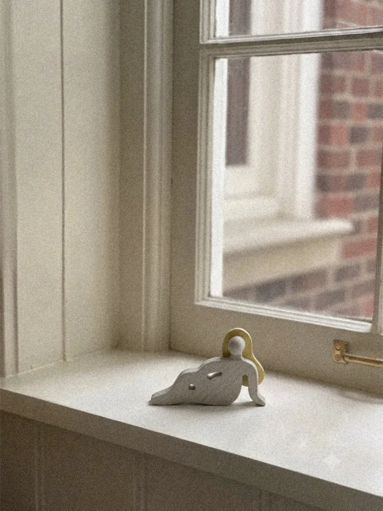 Kleine Holzfigur „Sense" aus der Women & Moods Kollektion von Babai Toys auf einer Fensterbank – eine liegende Figur in hellem Naturton mit goldfarbenem Haar.